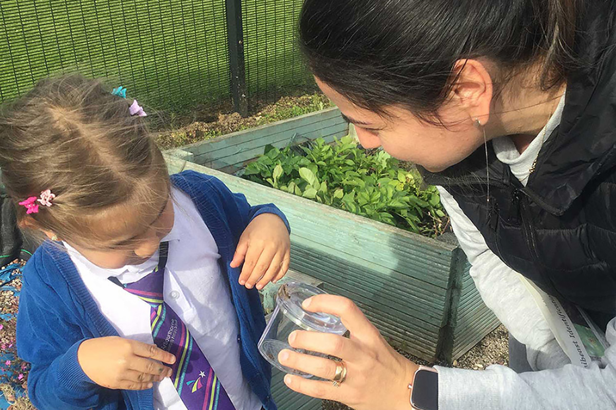 Child and adult in a garden looking at something they have found in a jar