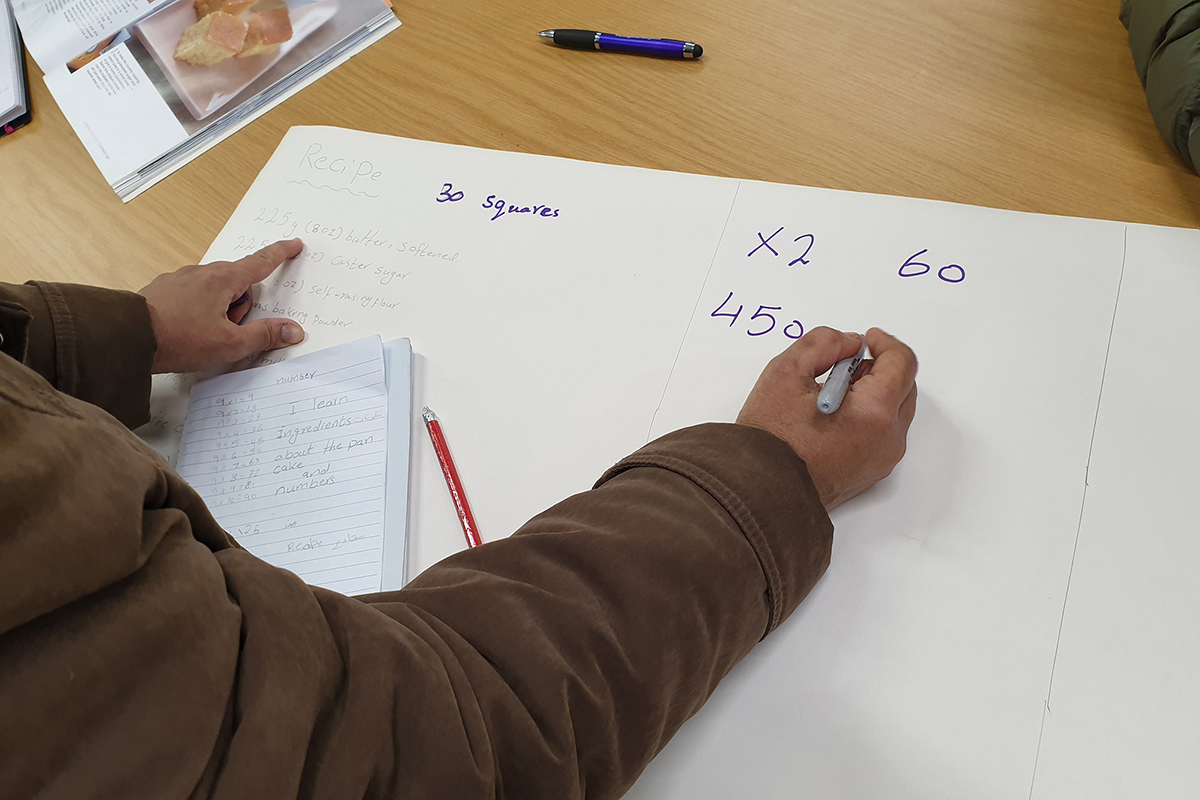 Learner working out a maths puzzle on a large sheet of paper