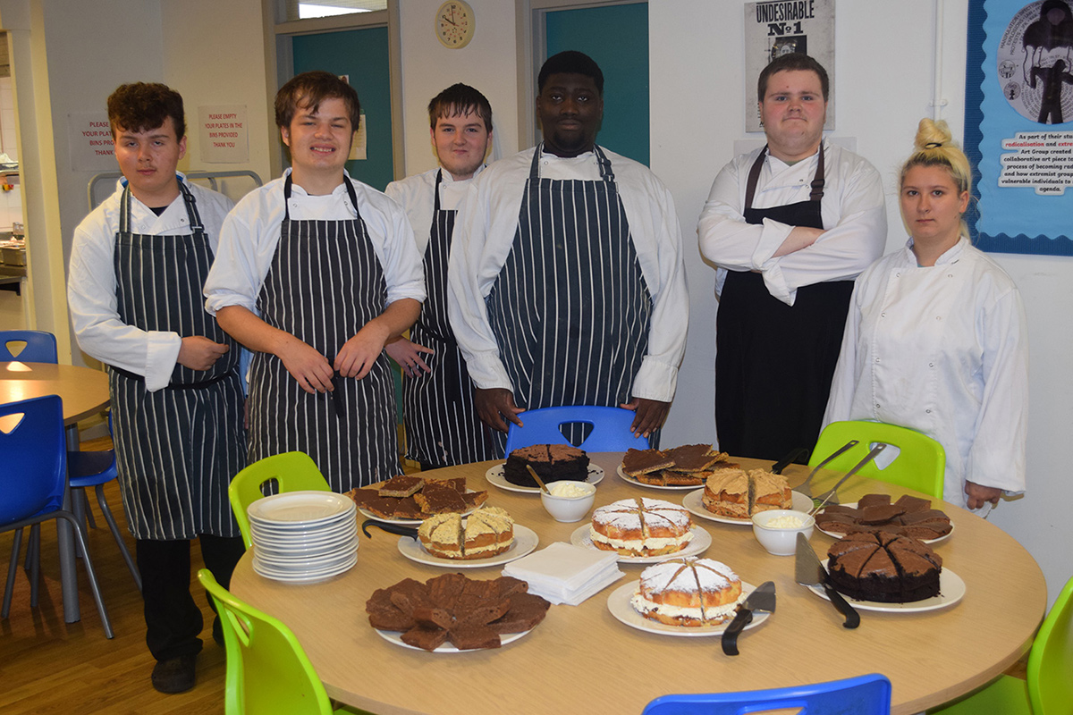 Students in chefs overalls standing at a table with baked goods