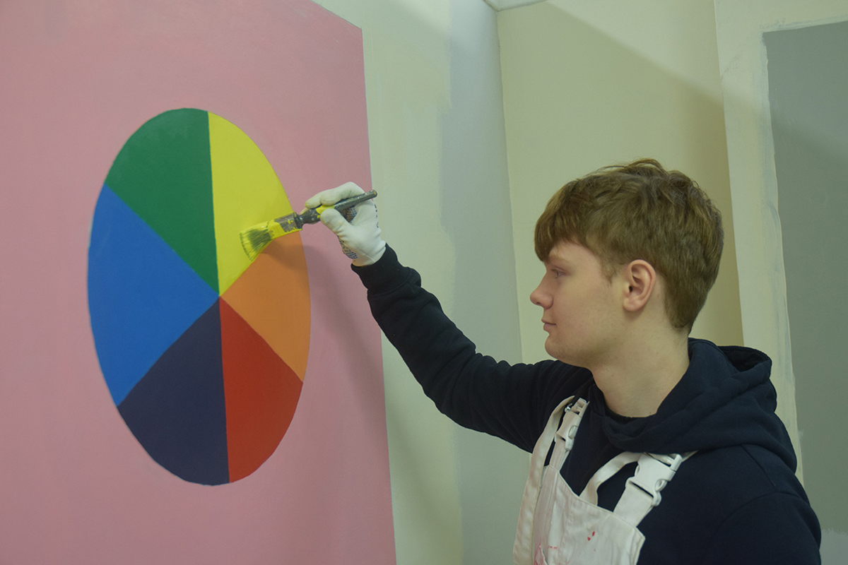 Learner painting a circle of rainbow colours onto a wall