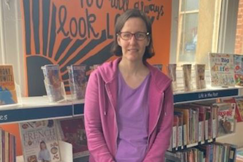 Anna F standing next to a bookshelf 